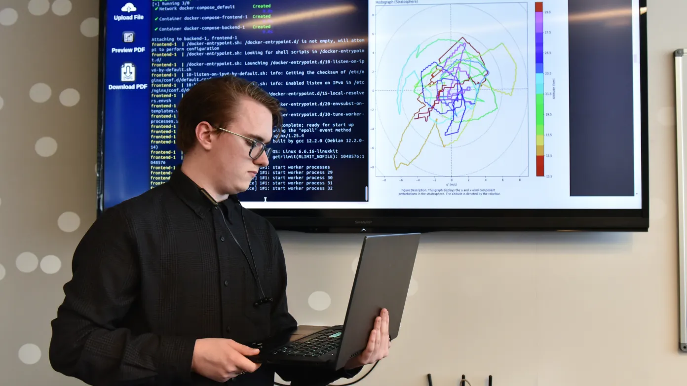 male student on a laptop with coding behind him on a screen