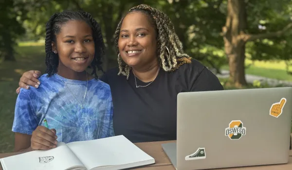 female adult learner in the park pose with her daughter while she works on her laptop
