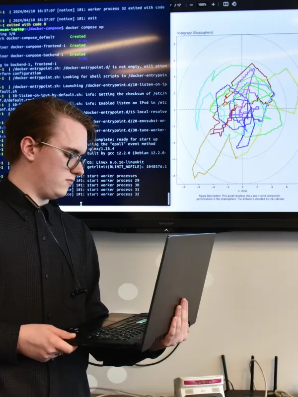 male student on a laptop with coding behind him on a screen