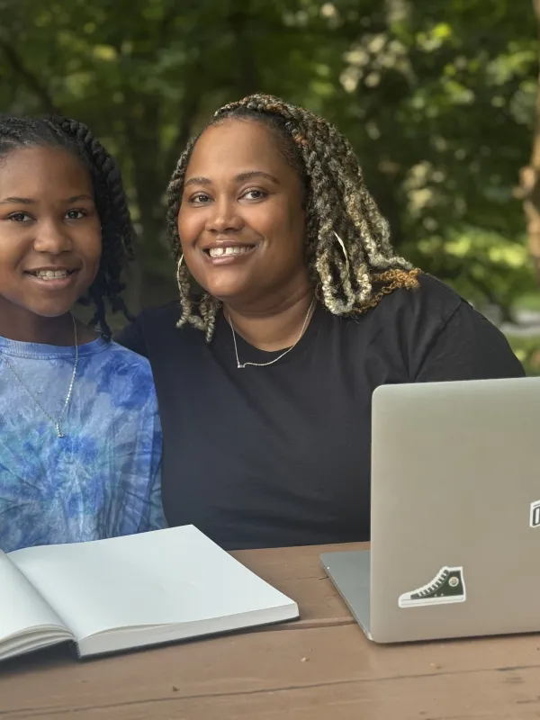 female adult learner in the park pose with her daughter while she works on her laptop
